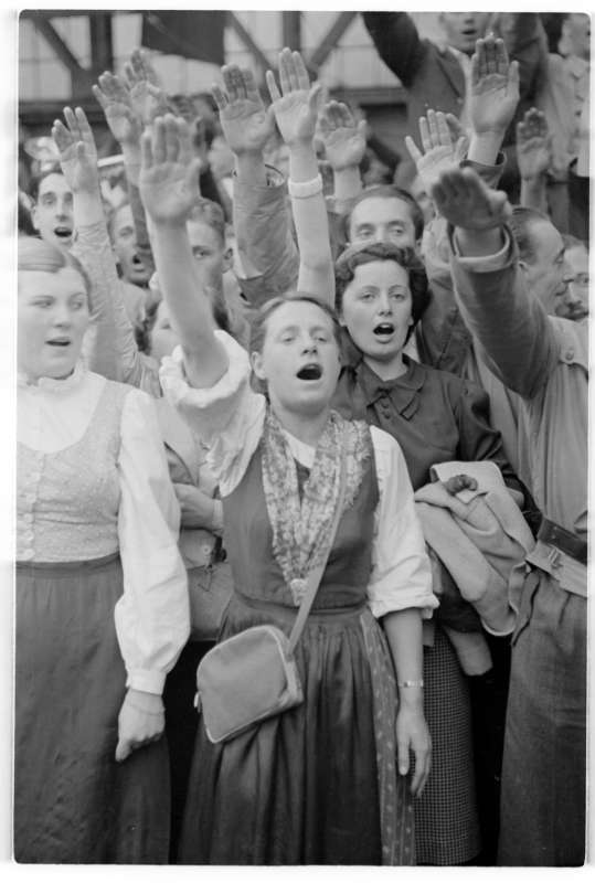 Schwarz-weiß-Foto: stehende Frauen, alle Hände zum Hitlergruß erhoben, rufen etwas.